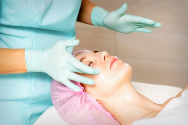 Eldivenli elleri olan kozmetolog kadın yüzüne krem sokan nemlendirici bir maske takıyor. Yüz kozmetolojisi tedavisi. Yüz bakımı prosedürleri