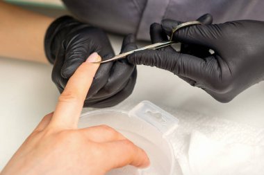 Manikür ustası, manikür salonunda koruyucu eldiven takan kadın tırnaklarından makas çıkartıyor.