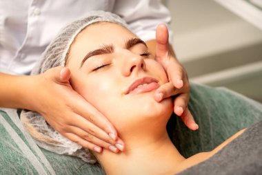 Yüz masajı. Güzel beyaz kadın spa salonunda gözleri kapalı yüz masajı yaptırıyor.