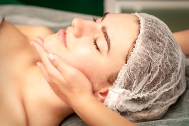 Yüz masajı. Spa salonunda genç beyaz bir kadının masaj yapan bir masörün elleri. Sağlık masajı konsepti.