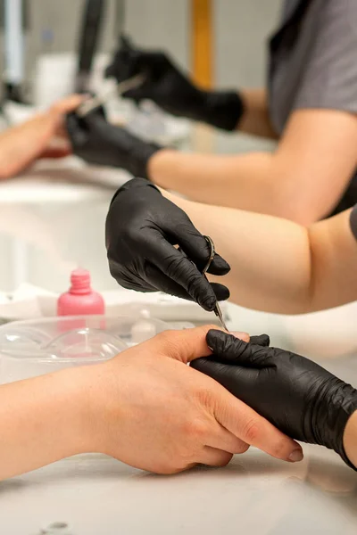 Manicure master removes cuticles from female nails with scissors wearing protective gloves in manicure salon