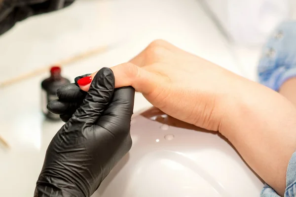 指甲清漆画 美容院一位美容师穿着橡胶黑色手套 在女性指甲上涂红色清漆的美容师的近照 — 图库照片