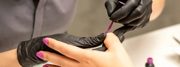 プロのマニキュア マニキュア師は 美容室で紫色のネイルポリッシュでクライアントの女性の爪を描いています 閉じます 美容業界のコンセプト — ストック写真