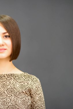 Kısa saçlı, esmer, güzel bir kadın. Gülümsüyor ve kameraya bakıyor. Koyu gri arka planda fotokopi çekiyor.