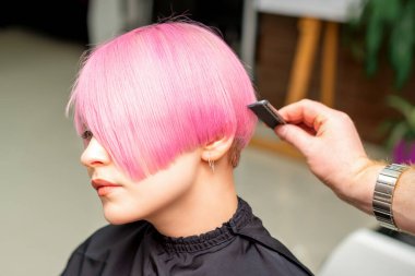 A hairdresser is combing the dyed pink short hair of the female client in a hairdresser salon