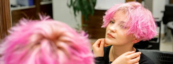 这位年轻美丽的高加索女人 有着一头新的短粉色的发式 她在镜子里看到了自己在理发店里检查发型的倒影 — 图库照片