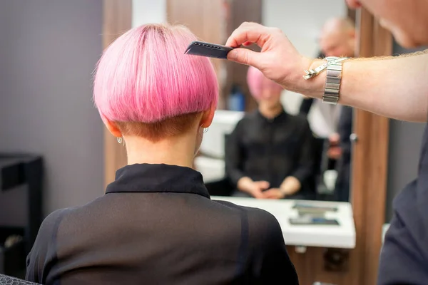 一位美发师正在理发店里梳理这位女顾客染成粉色的短发 这是后视镜 — 图库照片
