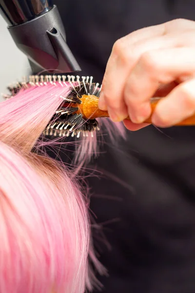 若い白人女性の短いピンクの髪を乾燥黒髪と黒丸みを帯びたブラシで髪サロンの男性の美容師の手で クローズアップ — ストック写真