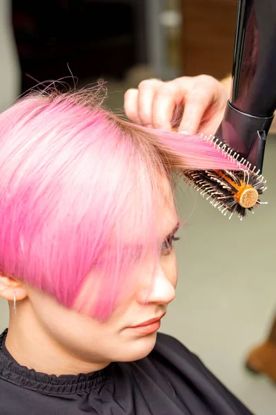 若い白人女性の短いピンクの髪を乾燥黒髪と黒丸みを帯びたブラシで髪サロンの男性の美容師の手で クローズアップ — ストック写真