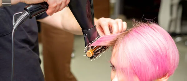 在美发厅里 用男性发型师的手 用黑色吹风机和黑色圆形刷子擦干年轻的高加索女人粉色短发 — 图库照片