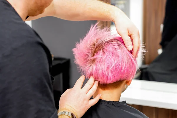 手付きの美容師はチェックアウトされ ヘアサロンで若い白人女性の短いピンクの髪型を固定しています — ストック写真