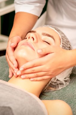 Facial treatment massage. Beautiful young caucasian woman with perfect skin receiving face and neck massage at a beauty spa