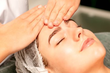 Kafa masajı. Kafkasyalı beyaz güzel bir kadın kaplıca salonundaki kapalı gözlerle kafa ve alın masajı yaptırıyor.