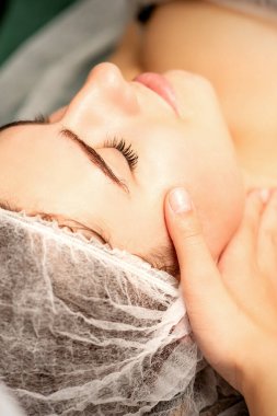 Yüz masajı. Spa salonunda genç beyaz bir kadının masaj yapan bir masörün elleri. Sağlık masajı konsepti.
