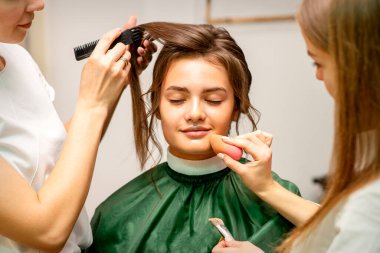 Makeup artist and hairdresser prepare the bride making hairstyle and makeup in a beauty salon