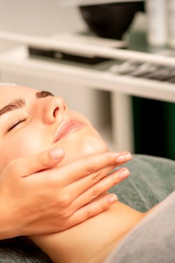 Yüz masajı. Spa salonunda genç beyaz bir kadının masaj yapan bir masörün elleri. Sağlık masajı konsepti.