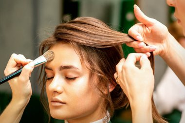 Makeup artist and hairdresser prepare the bride making hairstyle and makeup in a beauty salon