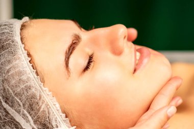 Yüz masajı. Spa salonunda genç beyaz bir kadının masaj yapan bir masörün elleri. Sağlık masajı konsepti.