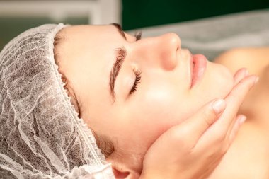 Yüz masajı. Spa salonunda genç beyaz bir kadının masaj yapan bir masörün elleri. Sağlık masajı konsepti.