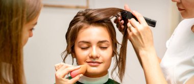 Makeup artist and hairdresser prepare the bride making hairstyle and makeup in a beauty salon