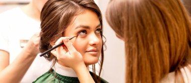 Makeup artist and hairdresser prepare the bride making hairstyle and makeup in a beauty salon