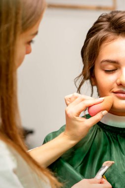 The makeup artist applies a cosmetic tonal foundation on the face using a cosmetic sponge