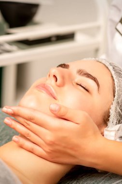 Yüz masajı. Spa salonunda genç beyaz bir kadının masaj yapan bir masörün elleri. Sağlık masajı konsepti.