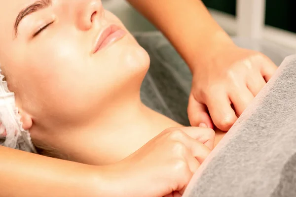 Massaging female breast, and shoulder. Young beautiful caucasian woman with closed eyes receiving chest and shoulders massage in beauty spa salon