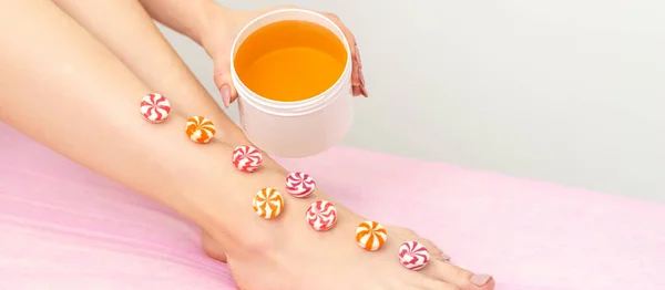 Depilation, waxing concept. Round candies lying down in a row on the female leg with a jar of sugar paste, close up
