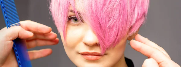 手と櫛を持つ美容師はチェックアウトされ ヘアサロンで若い白人女性の短いピンクの髪型を固定しています — ストック写真