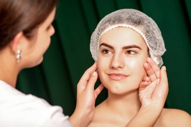 Plastic surgery and beauty concept. Professional cosmetician examining and touching the face of the beautiful young caucasian smiling woman in a clinic of esthetic cosmetology