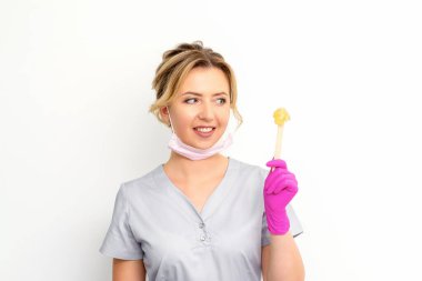 Şekerleme uzmanının elinde sıvı sarı şeker macunu var. Beyaz arka plandaki tahta bir çubukta tüy dökmek için balmumu.