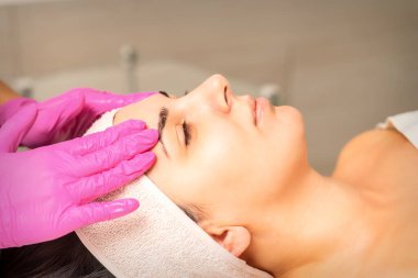 Eldivenli elleri olan kozmetolog kadın yüzüne krem sokan nemlendirici bir maske takıyor. Yüz kozmetolojisi tedavisi. Yüz bakımı prosedürleri