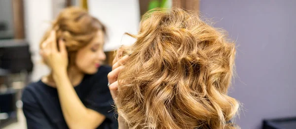 在理发店的镜子前 年轻女人正在检查她新的卷曲棕色的发式 — 图库照片