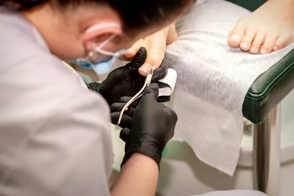 Professional pedicure. Pedicure master wearing latex gloves cuts female toenails in the beauty salon, closeup