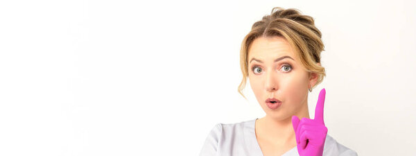 Молодая белая женщина-врач в розовых перчатках, указывая указательным пальцем вверх, делает жест указательным пальцем. У меня есть идея.