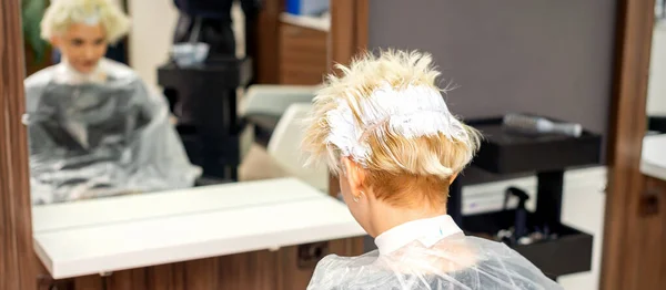 一位年轻的高加索金发女子坐在美发店前 用染发剂把她的头发染成了白色 — 图库照片