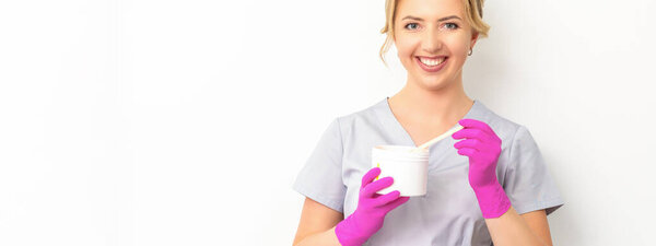 Портрет женщины-кавказского косметолога, держащей банку сахарной пасты для сахарирования в розовых перчатках на белом фоне