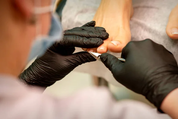 Professional pedicure. Pedicure master wearing latex gloves cuts female toenails in the beauty salon, closeup