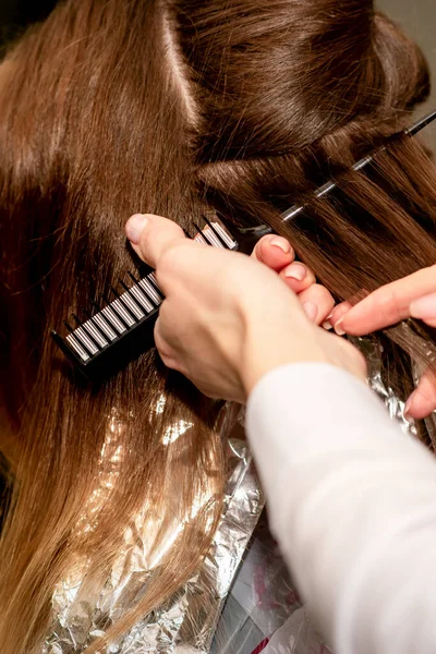 Hairdresser\'s hands prepare brown hair for dyeing with a comb and foil in a beauty salon, close up