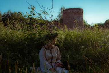 Pagan çelengi içindeki genç kadın otlar içinde