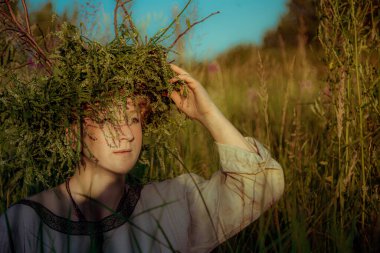 Pagan çelengi içindeki genç kadın otlar içinde