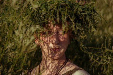 Pagan çelengi içindeki genç kadın otlar içinde