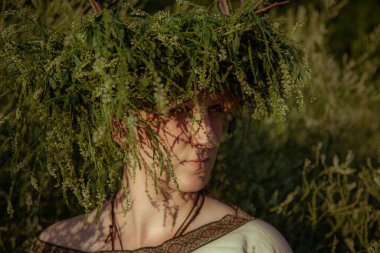 Pagan çelengi içindeki genç kadın otlar içinde