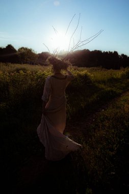 Gün batımında pagan çelengi giymiş genç bir kadın dans ediyor.