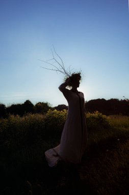 Gün batımında pagan çelengi giymiş genç bir kadın dans ediyor.