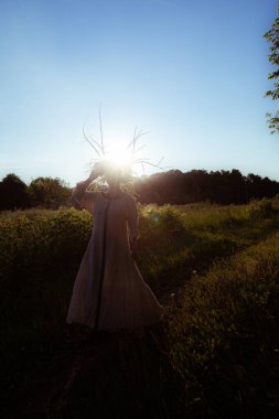 Gün batımında pagan çelengi giymiş genç bir kadın dans ediyor.