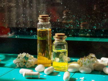 İki şişe yağ, ilacın yanında, koyu bir zemin ve bir damla su üzerinde. Alternatif tıp kavramı