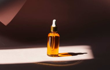 Işık arka planında damlatıcısı olan gerekli yağ şişesinin yakın plan çekimi.