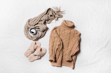 Sıcak eşarp, örgü süveter, bir fincan kahve ve beyaz arka planda terlikler.